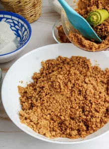 Witte kom gevuld met fijn gemalen koekkruimels, klaar voor gebruik als basis voor de dadel cheesecake.